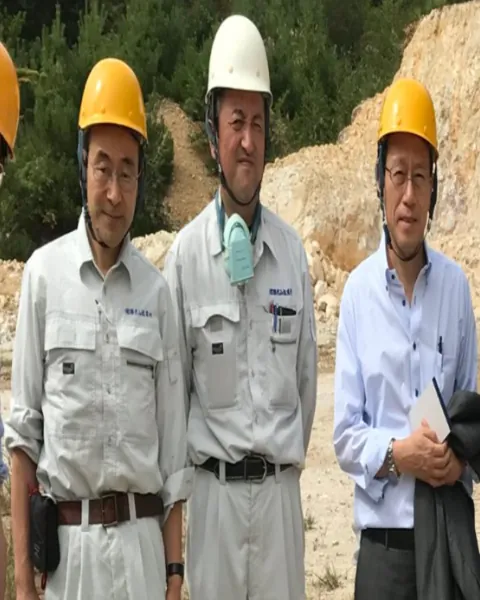 Three Japanese technical experts in helmets at a mine site.