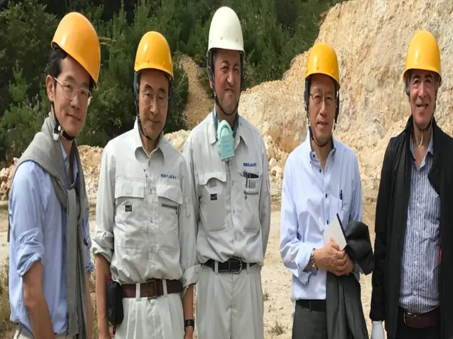 Five Japanese technical experts in helmets at a quarry site.