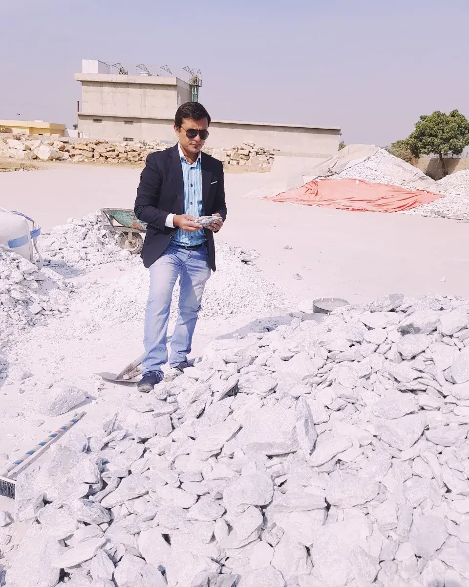 Manager standing on a white mineral stockyard in front of processing sheds.
