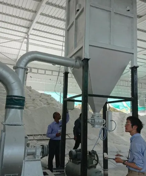Three men inspecting a mill and cyclone assembly in a processing shed.