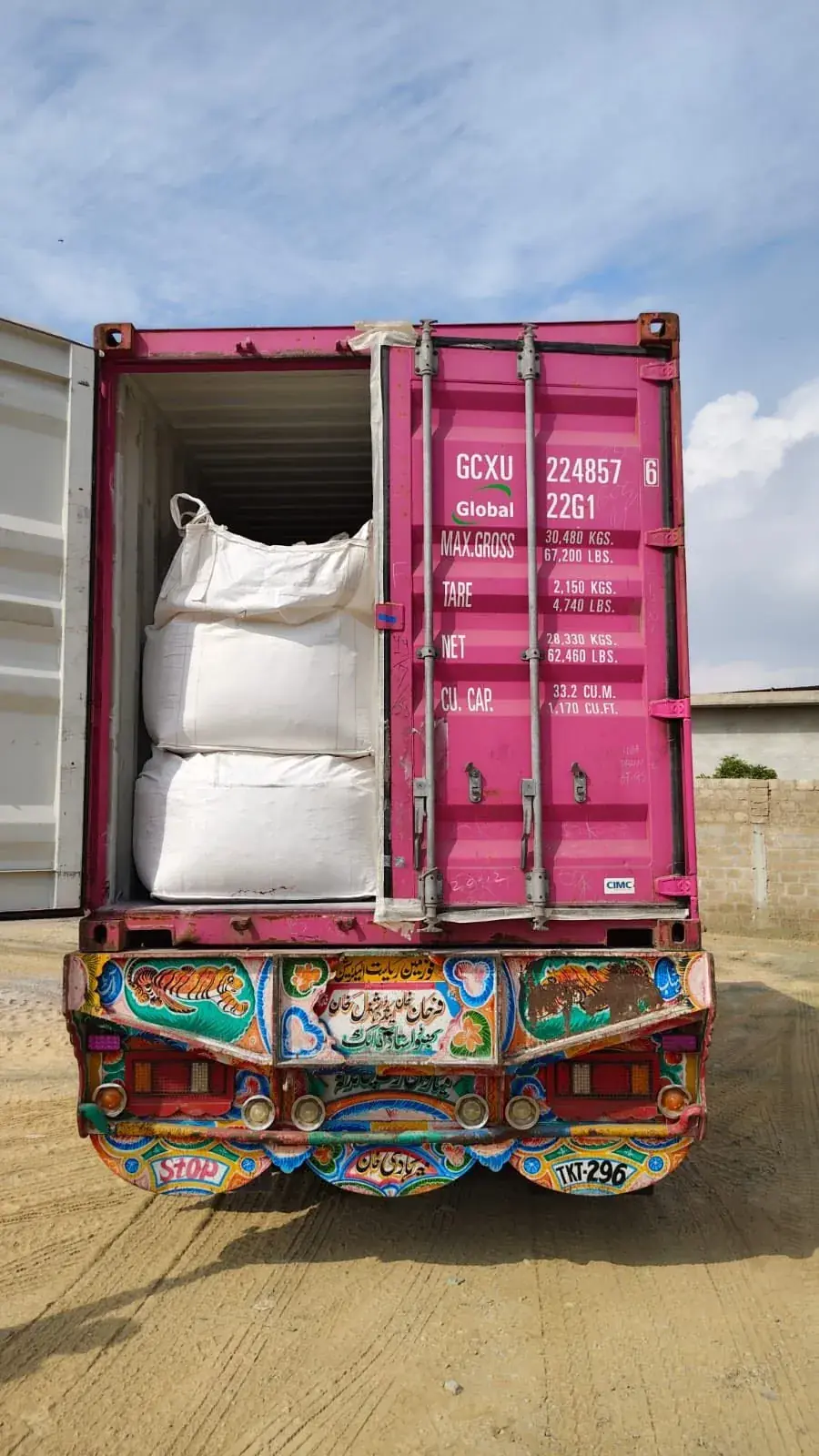 Decorated Pakistani truck carrying a pink shipping container filled with jumbo bags.