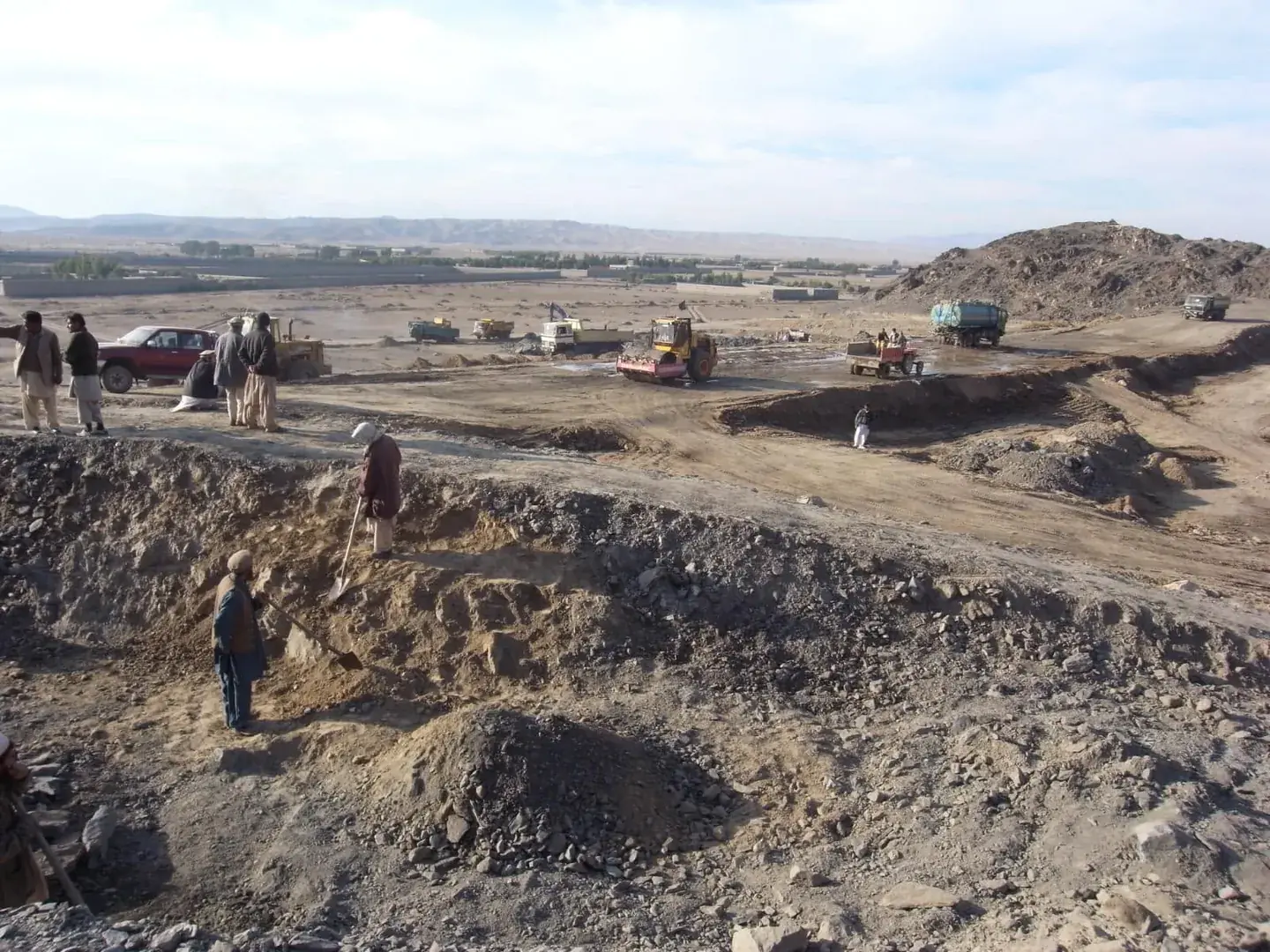 Wide view of an excavation site with workers and trucks on bare ground.