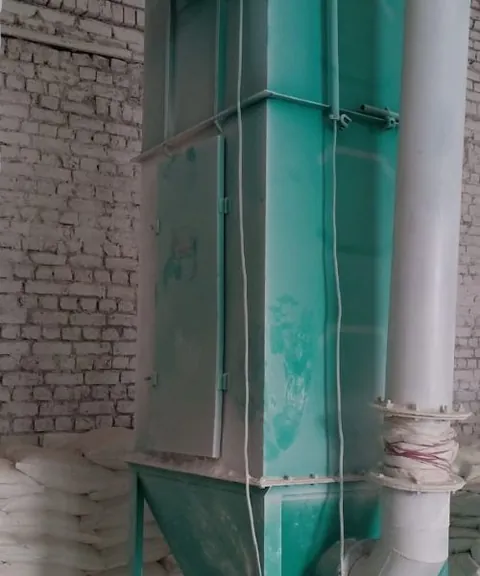 Teal duct and filter column beside bagged product in a processing shed.