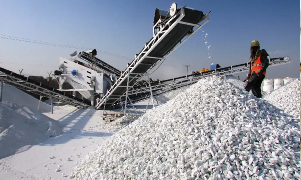Conveyor stacker discharging crushed white talc onto a stockpile, with a worker in the foreground.