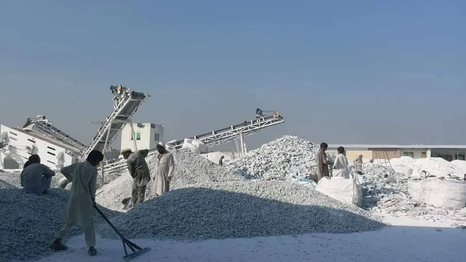 Screening plant with conveyors and white talc stockpiles, workers shovelling in the foreground.