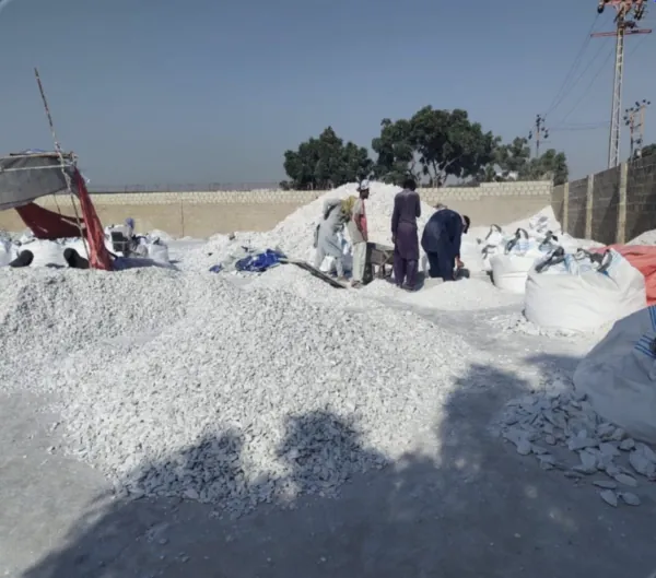 Men sorting white talc lumps in a walled yard beside bulk bags.