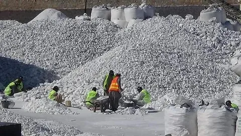 Workers in safety vests sorting white talc lumps between large stockpiles and bulk bags.