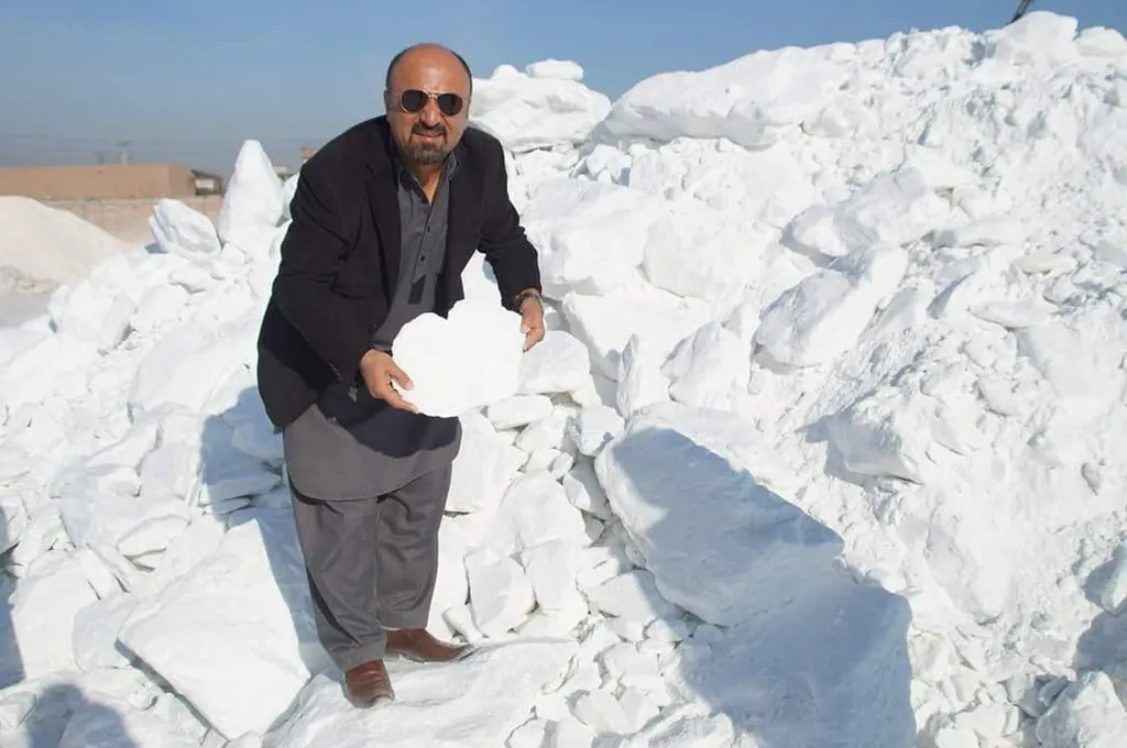 Man holding a large white talc lump on top of a talc stockpile.