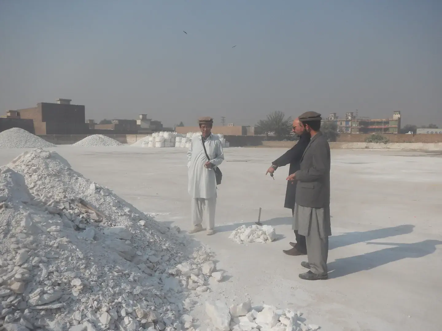 Two men standing in a yard of white talc lump stockpiles.