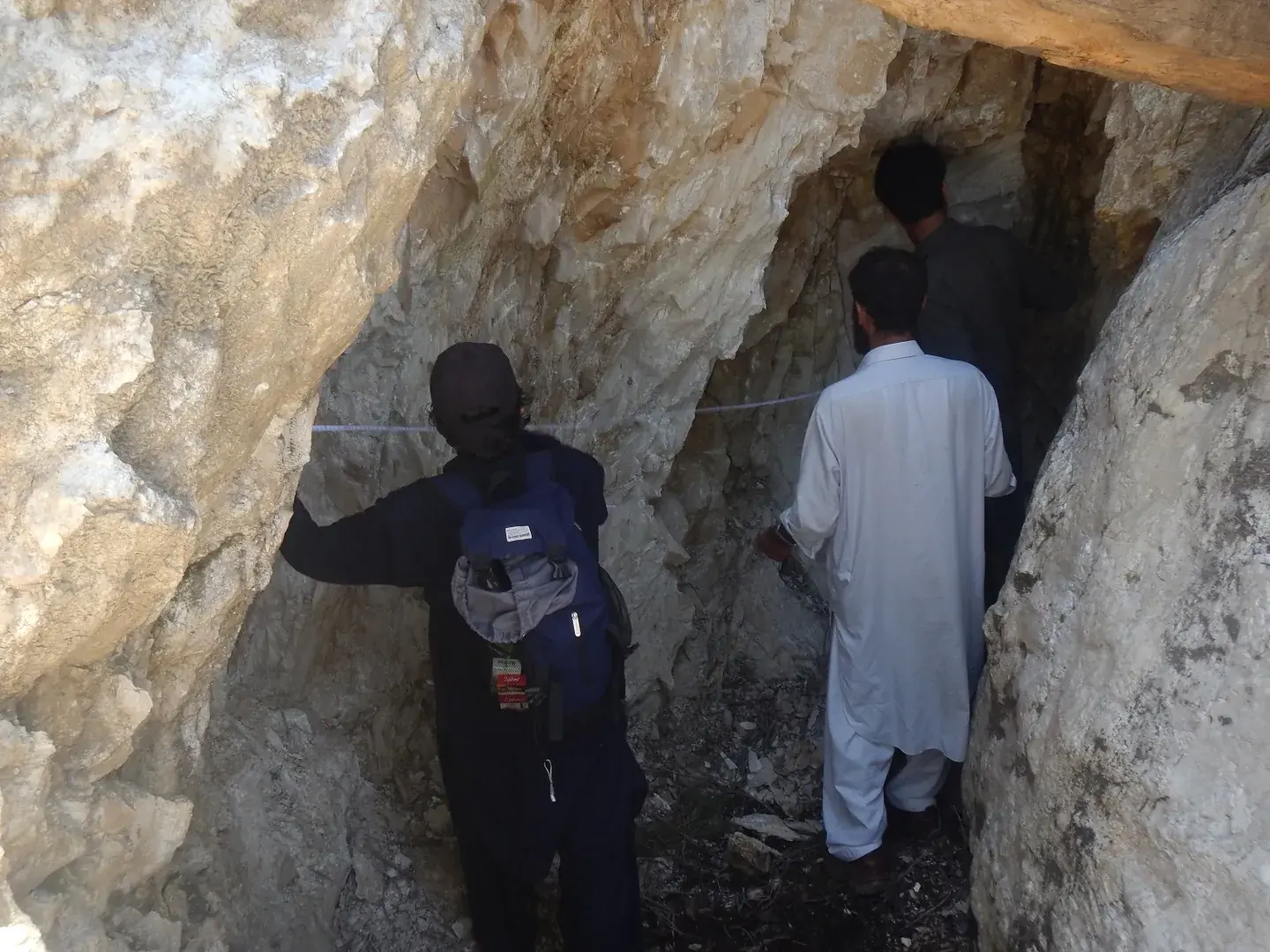 Men inspecting the walls of a pale rock adit.
