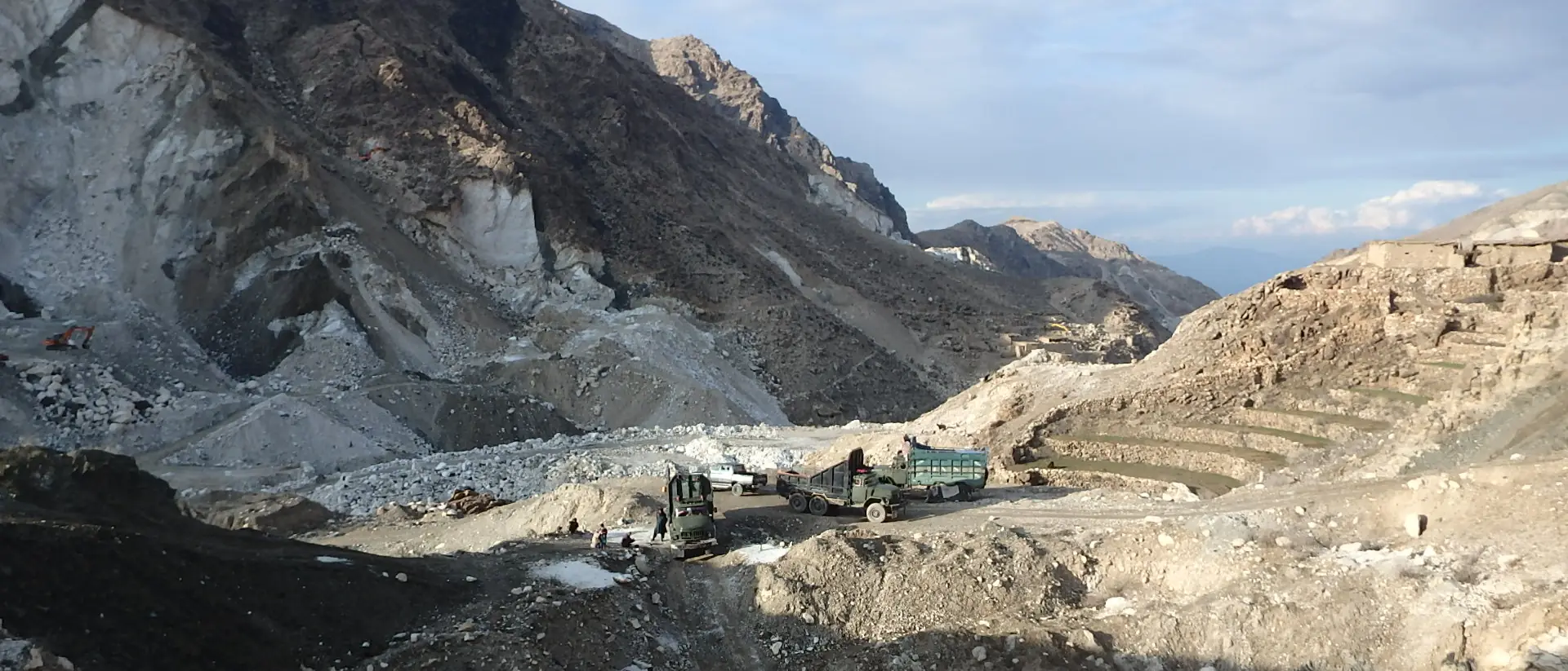 Excavator and truck working on the terraced benches of an open-pit mine in arid mountains.