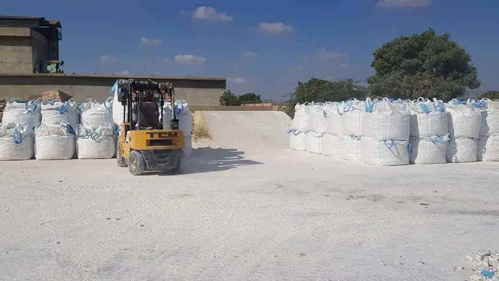 Rows of filled white jumbo bags in an open storage yard with a forklift.