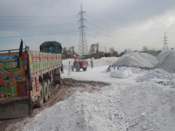 Decorated truck parked beside white talc stockpiles at the Peshawar warehouse yard.
