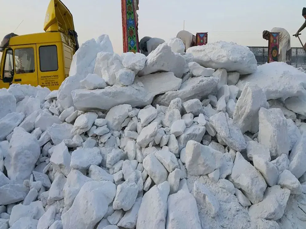 Pile of white talc lumps beside a yellow truck being loaded.