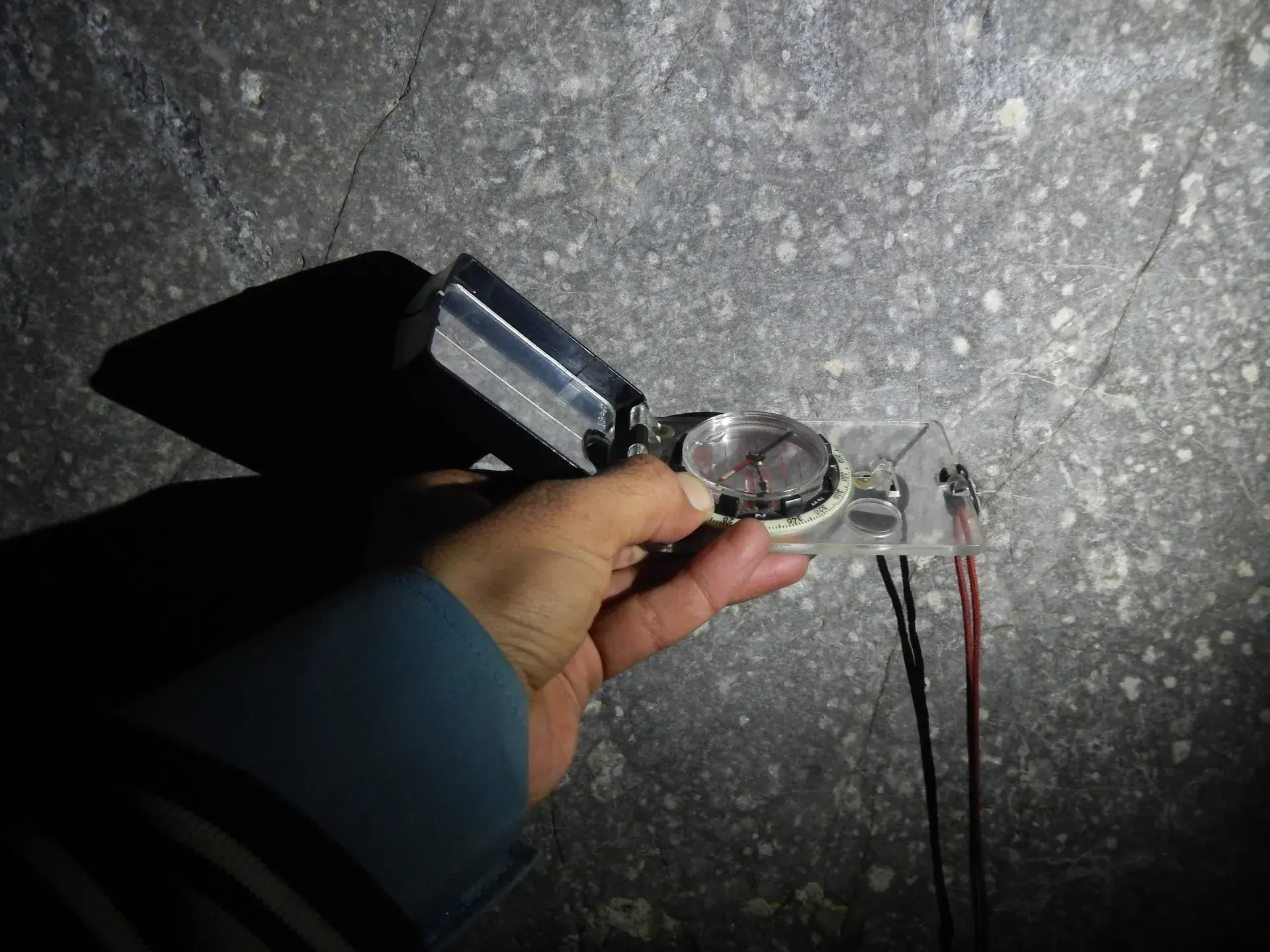 Hand holding a geological compass-clinometer to measure rock orientation in low light.