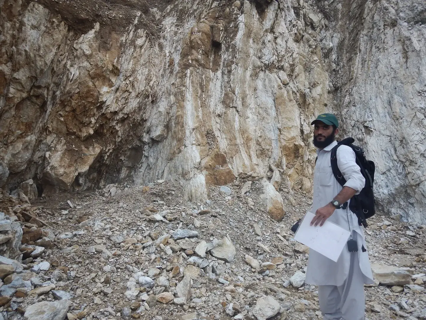 Geologist with backpack and field notes standing at a white rock face.