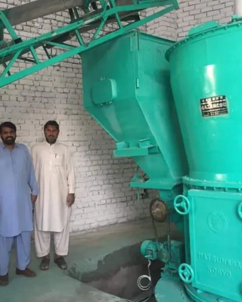 Two staff standing beside a teal grinding mill in a brick processing shed.