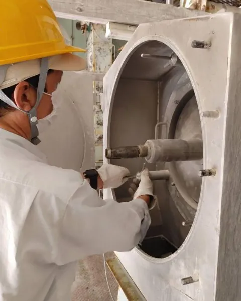 Worker in helmet and mask servicing the grinding chamber of a mill.