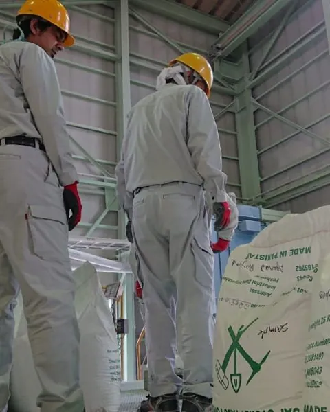 Two workers in white uniforms and helmets beside bagged product in a processing plant.