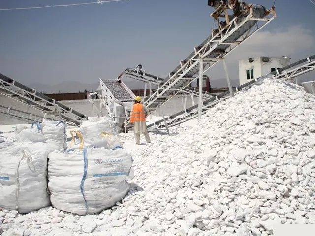 Conveyor stackers building a stockpile of crushed white talc, with jumbo bags and a worker nearby.