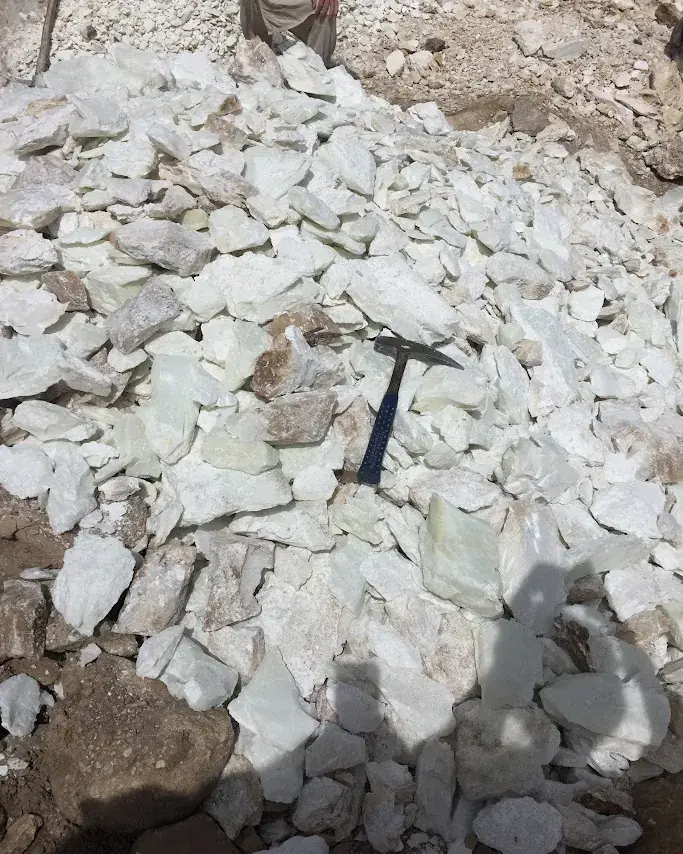 White talc fragments with a geological hammer resting on top at a field site.