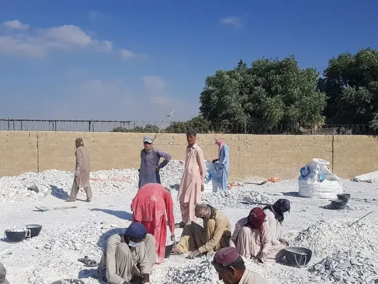 Workers sorting white talc lumps by hand in a walled yard.