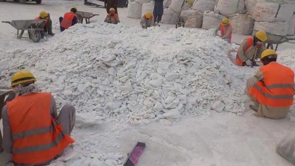 Workers in hard hats and safety vests sorting white talc lumps beside filled bulk bags.