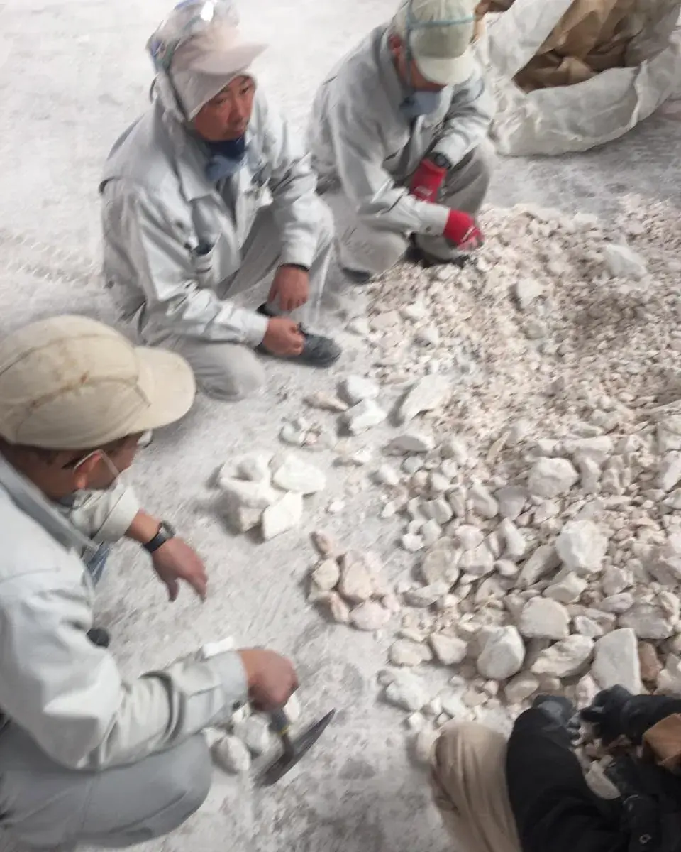 Two inspectors in uniforms and caps checking white talc lumps with a worker during hand sorting.