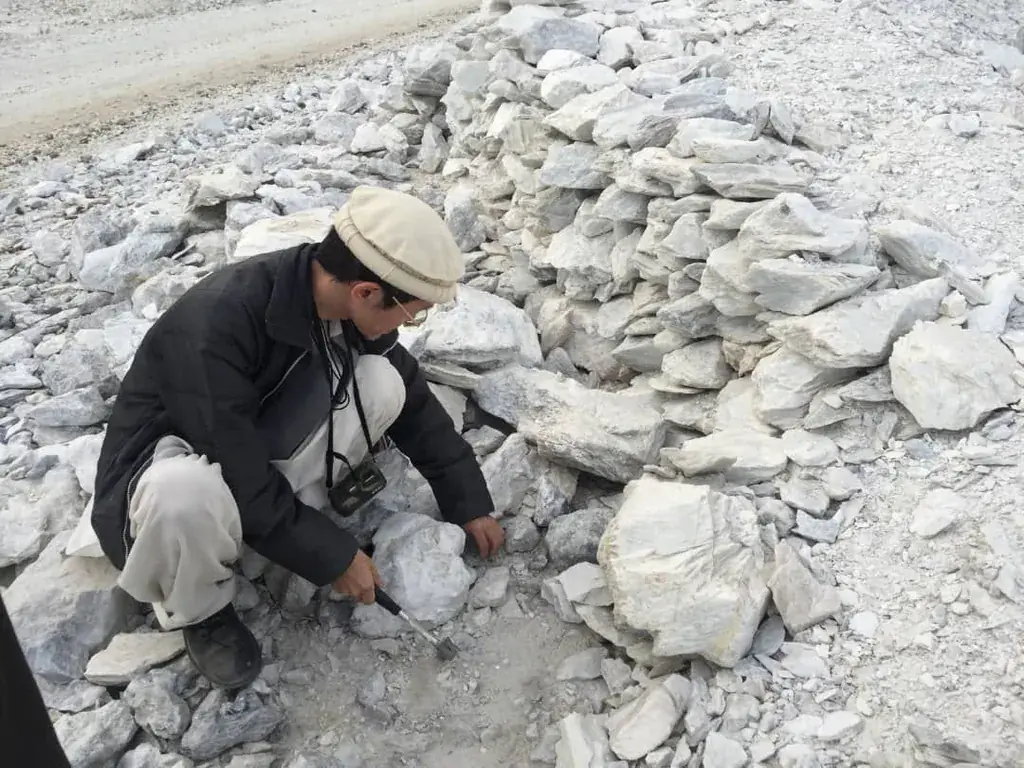 Man crouching to inspect a pile of white talc lumps.