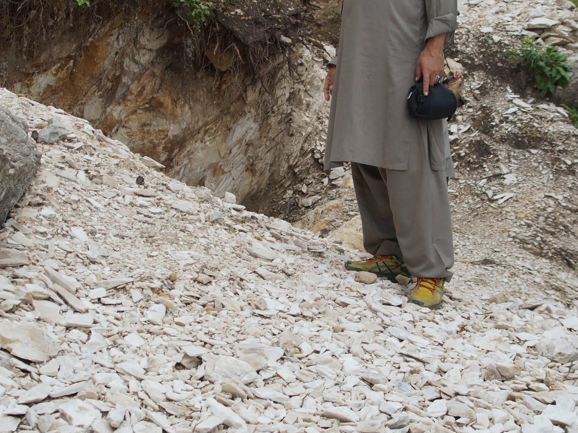 Man standing on a slope of flat white talc fragments below a rock outcrop.