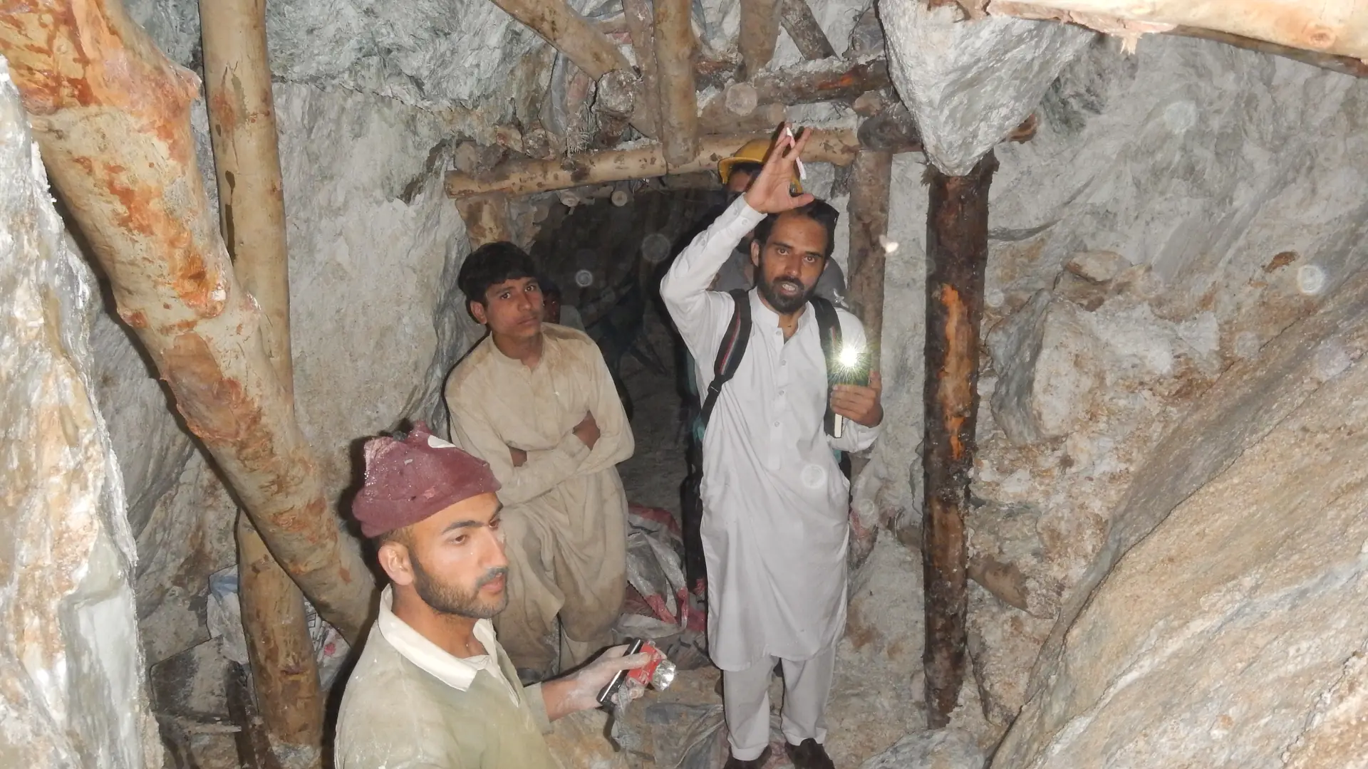 Miners inside a timber-supported underground adit, one holding a headlamp.