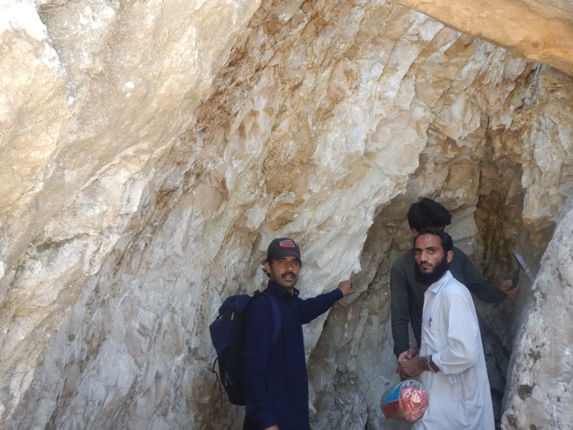 Two men inspecting the pale rock walls inside an underground working.