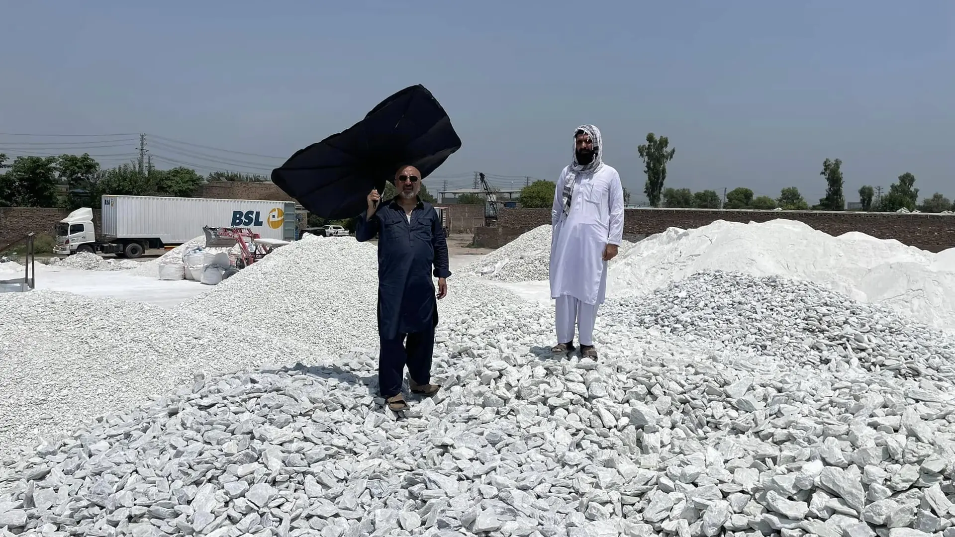 Men working on a stockpile of white talc lumps, one carrying a sack, with a truck behind.